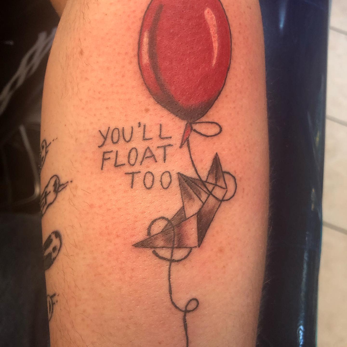 Minimalist Pennywise tattoo with a red balloon, paper boat, and "You'll Float Too" text